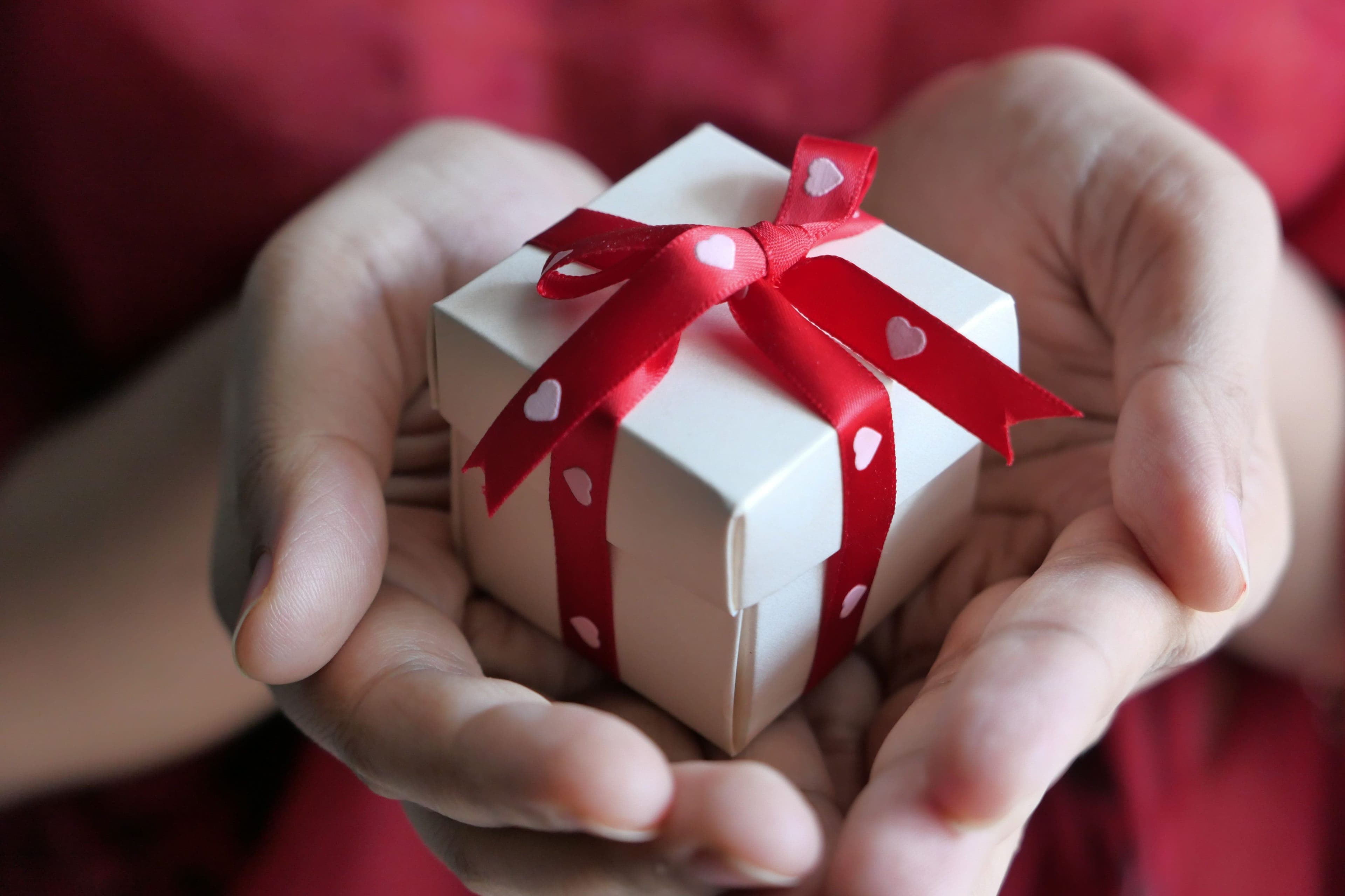 Invité tenant au creux des mains une boîte cadeau nouée d'un ruban rouge, prête à être offerte aux mariés