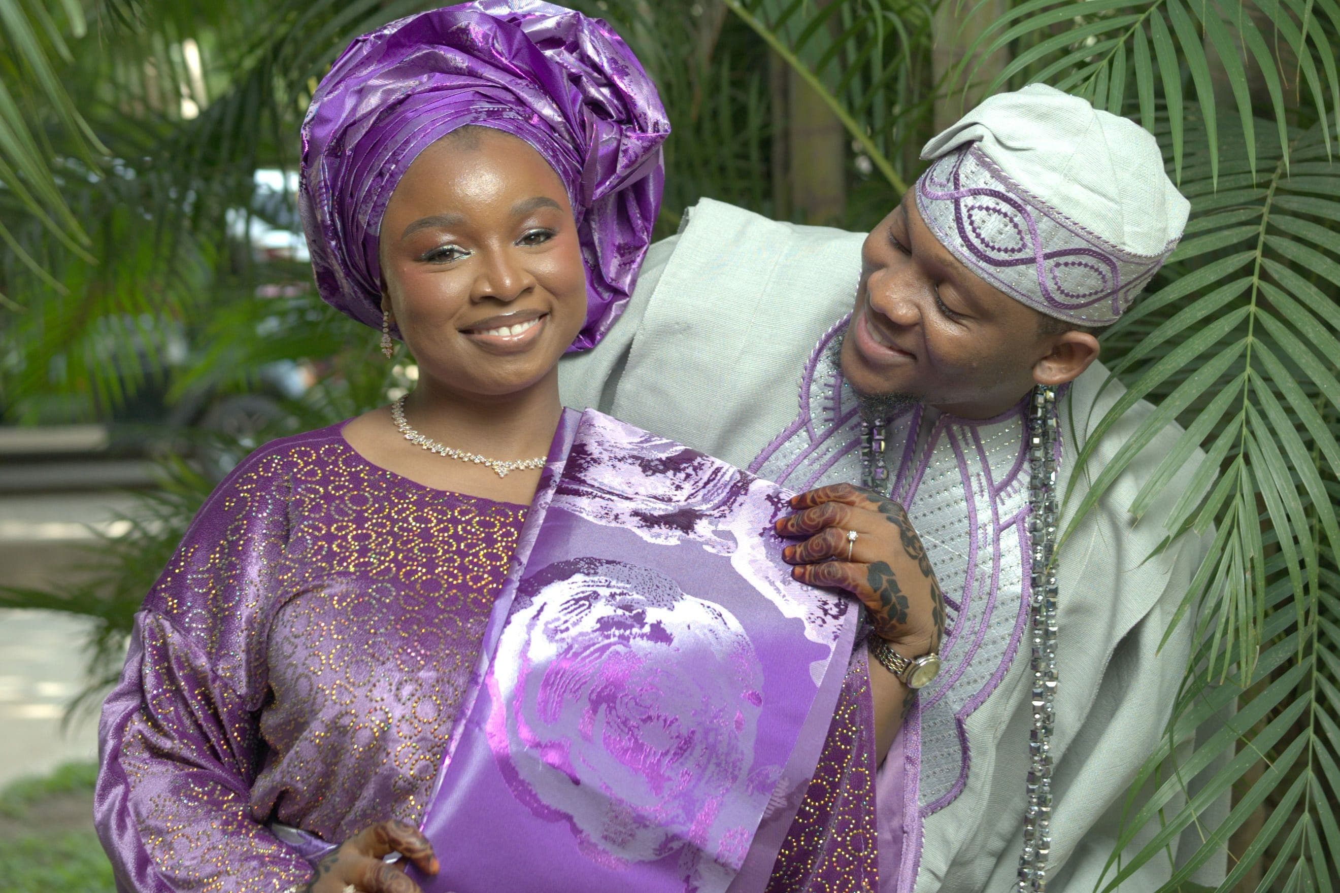 Couple de mariés souriants en tenues traditionnelles africaines, la mariée coiffée d'un foulard violet