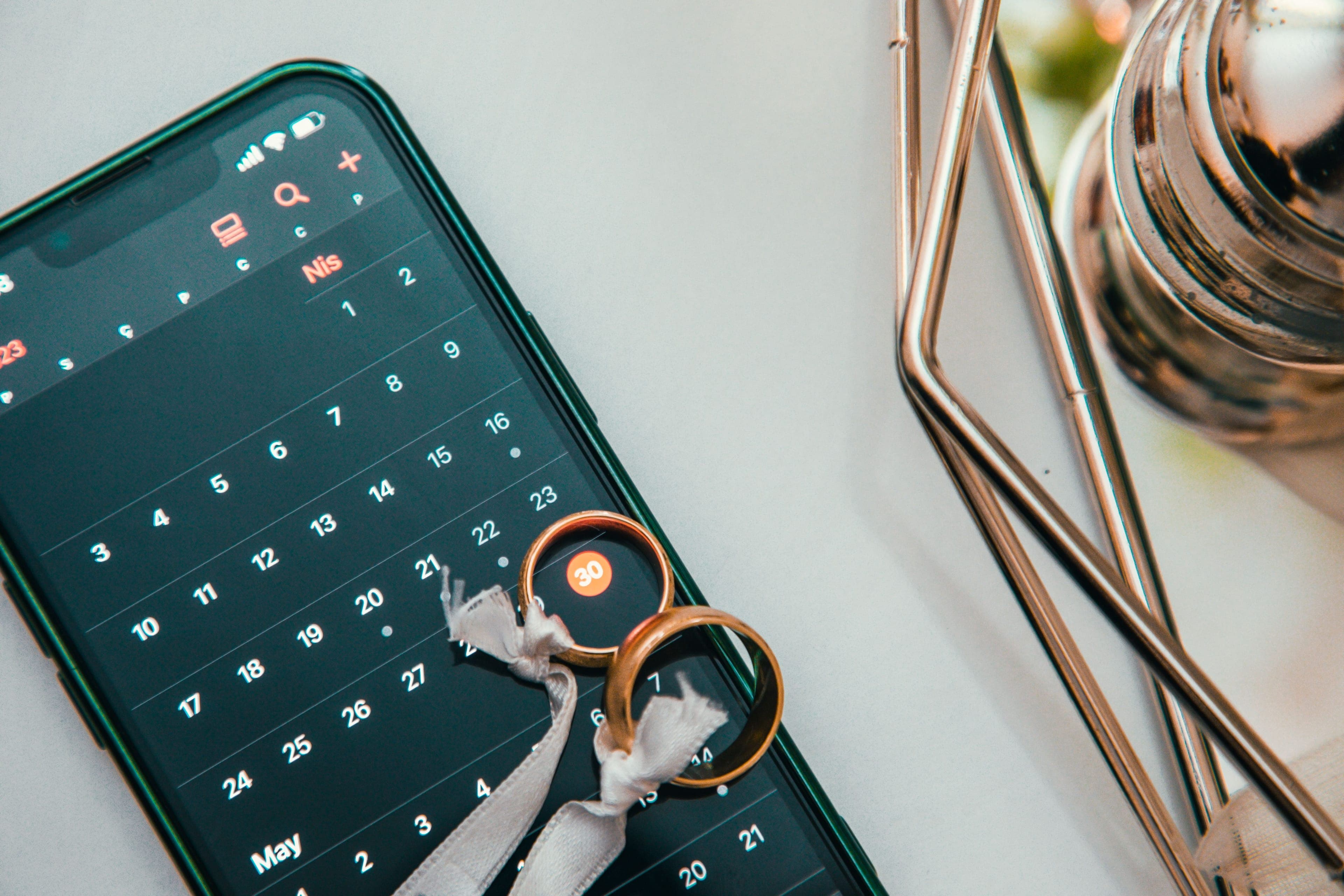 Deux alliances posées sur un smartphone affichant un calendrier, pour choisir la date du mariage