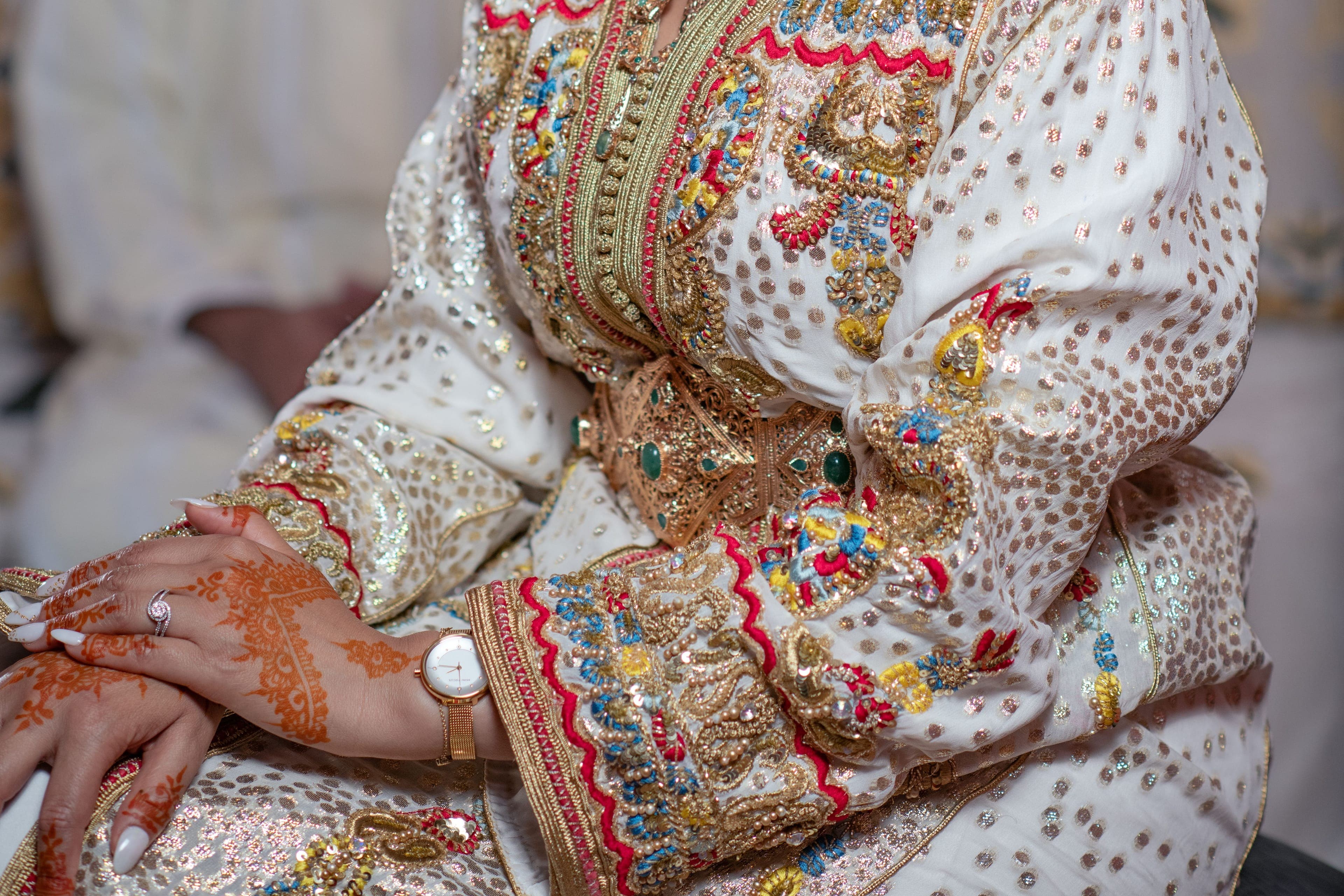 Caftan de mariée blanc brodé d'or et ceinture ornée, mains décorées de henné