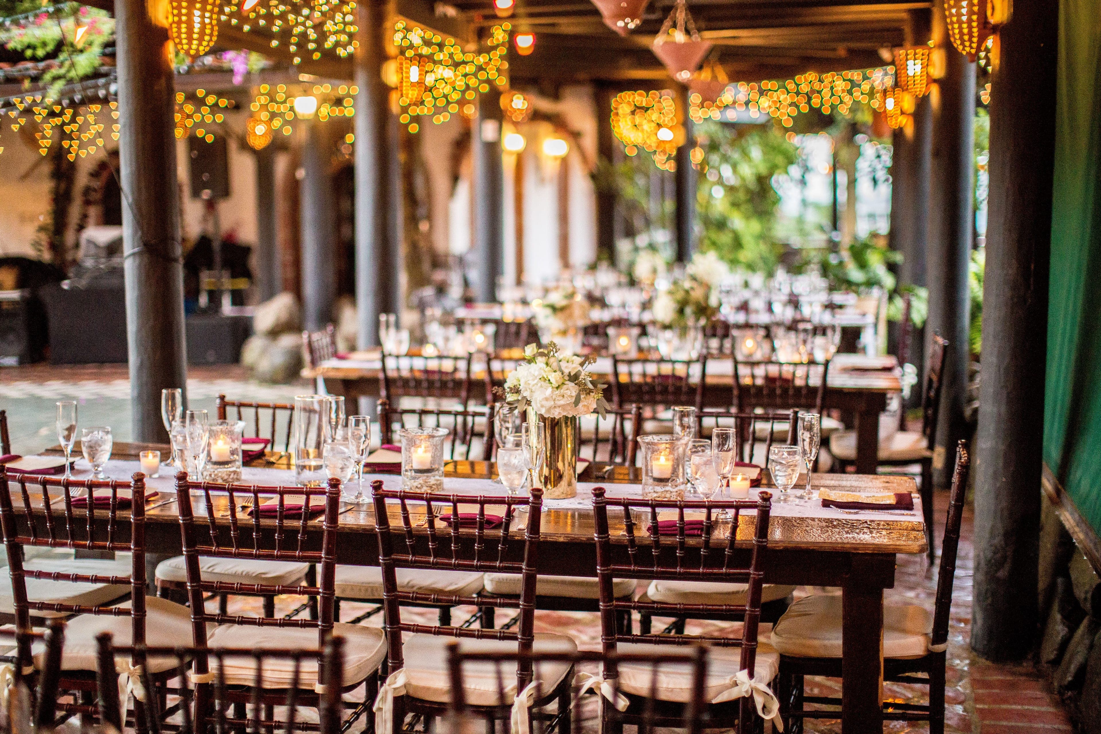 Salle de réception dressée pour le dîner du mariage, tables en bois et guirlandes lumineuses