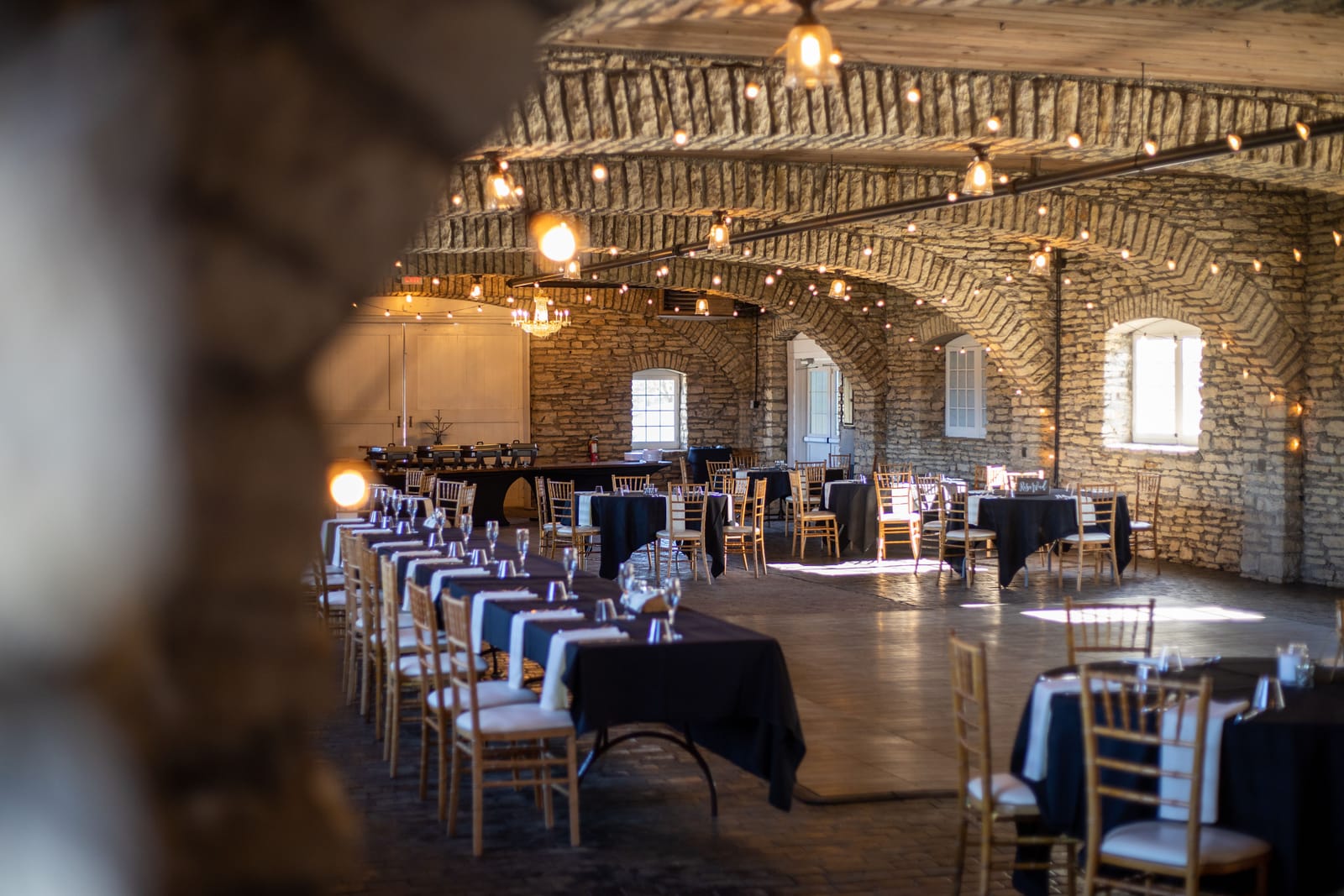 Salle de réception aux murs de pierre et aux arches voûtées, avec tables dressées et chaises en bois