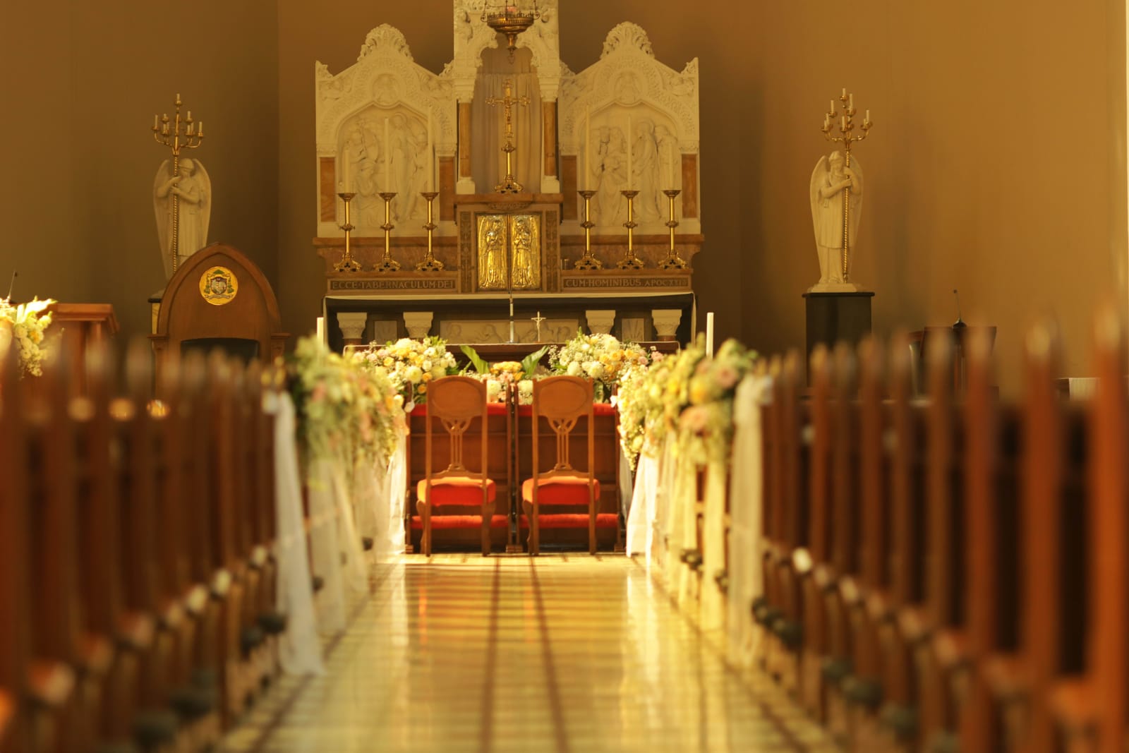 Allée d'église bordée de bouquets clairs, avec deux chaises rouges pour les mariés devant l'autel