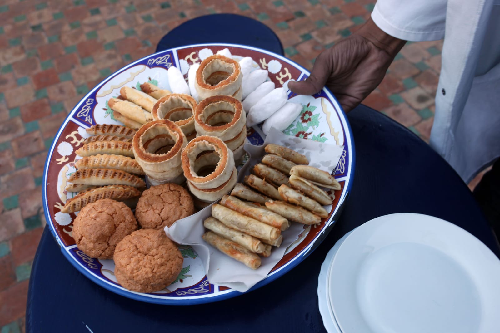 Plateau de pâtisseries marocaines traditionnelles servi sur une table, à côté d'une pile d'assiettes blanches