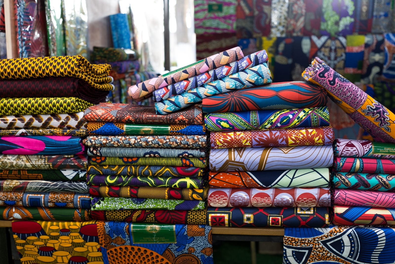 Piles de tissus imprimés aux motifs colorés sur l'étal d'un marché d'Afrique de l'Ouest