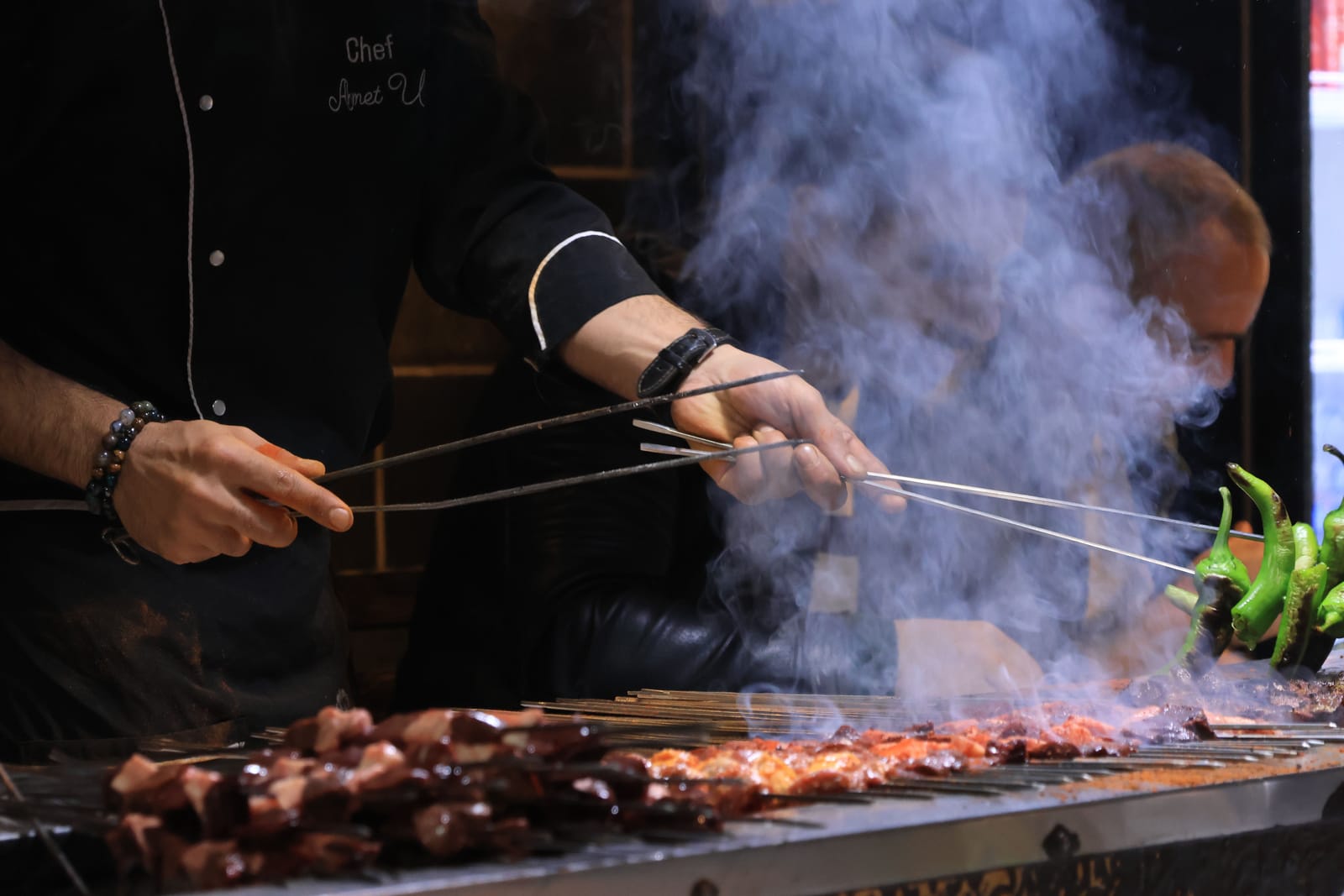 Cuisinier grillant des brochettes de viande et de légumes au-dessus des flammes, dans la fumée